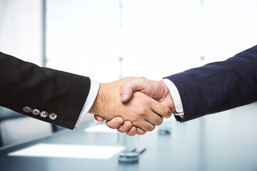Two businessmen shake hands on the background of bright conference room, investing concept, close up