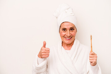 Middle age caucasian woman wearing a bathrobe holding toothbrush isolated on white background smiling and raising thumb up