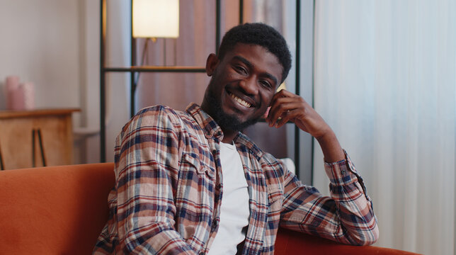 Handsome candid happy casual calm young african american bearded man smiling friendly, glad expression, looking away dreaming resting, feel satisfied concept, sitting on sofa at home in living room