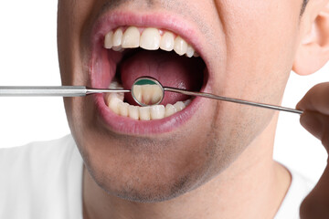 Examining man's teeth and gums with dentist's tools on white background, closeup