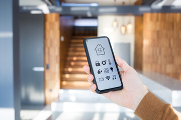 man controls smart home devices using app for mobile phone on background of interior of house. concept of digitalization. a mockup with hand holding phone