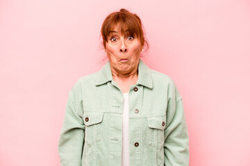 Middle age caucasian woman isolated on pink background shrugs shoulders and open eyes confused.