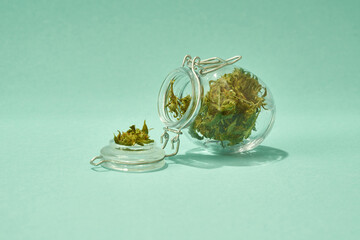 Glass jar with dry marijuana on green background