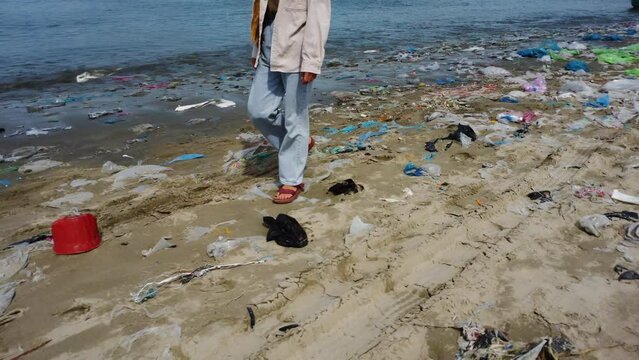 Woman Walking Along a Polluted Beach with Plastic Waste in Mui Ne, Vietnam with Tracking Shot.