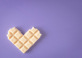 White chocolate in the shape of heart on purple background. A sweet gift for love day.