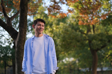 smiling handsome Asian young man at forest in autumn