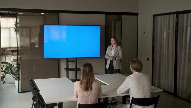 Diverse office conference room meeting: female project manager uses Chroma Key wall mounted blue screen TV to present an investment project. Project presentation. Business concept, training