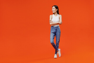 Fototapeta na wymiar Full size excited jubilant exultant cheerful happy young woman of Asian ethnicity 20s years old in white tank top hold hands crossed looking aside isolated on plain orange background studio portrait.