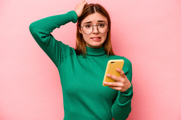 Young caucasian woman holding mobile phone isolated on pink background being shocked, she has...
