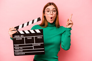 Young caucasian woman holding a clapperboard isolated on pink background having some great idea,...