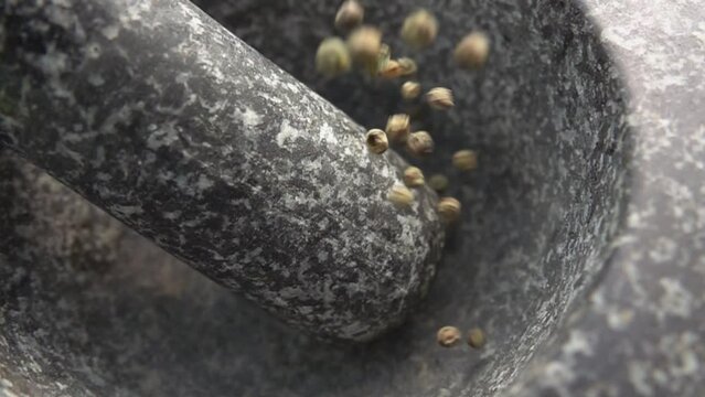Close-up of the spicy grey peppercorns falling into the grey stone mortar