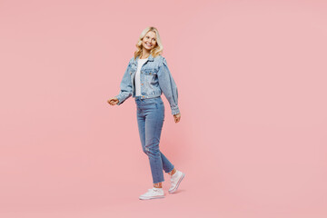 Full body elderly smiling cheerful fun happy woman 50s wearing denim jacket walking going look aside isolated on plain pastel light pink background studio portrait. People lifestyle fashion concept.