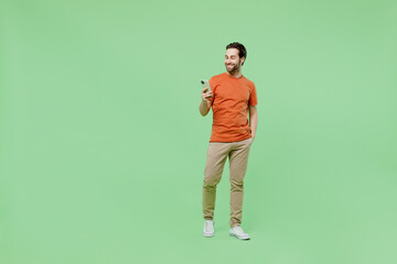 Full body young smiling happy fun man 20s wear casual orange t-shirt hold in hand use mobile cell...