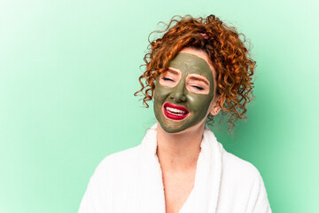 Young red hair woman with a facial aloe vera mask after a bath isolated laughing and having fun.