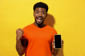 Young man of African American ethnicity 20s in orange t-shirt hold in hand use mobile cell phone...