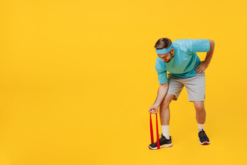 Fototapeta premium Full body side view young fitness trainer instructor sporty man sportsman wear headband blue t-shirt use fitness elastic bands for hands isolated on plain yellow background. Workout sport concept