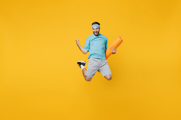 Fototapeta na wymiar Full body overjoyed young fitness trainer instructor sporty man sportsman in headband blue t-shirt hold yoga mat jump high do winner gesture isolated on plain yellow background. Workout sport concept