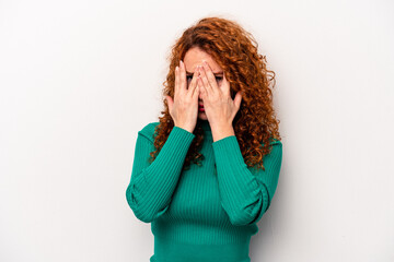 Young ginger caucasian woman isolated on white background blink at the camera through fingers, embarrassed covering face.