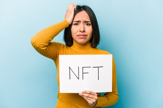 Young hispanic woman holding NFT placard isolated on blue background being shocked, she has remembered important meeting.
