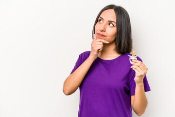 Fototapeta premium Young hispanic pregnant woman holding pacifier isolated on white background looking sideways with doubtful and skeptical expression.