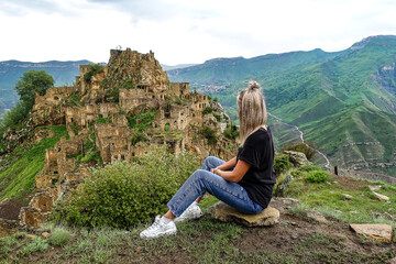 Naklejka premium A girl on the background of Gamsutl village in the Caucasus mountains, on top of a cliff. Dagestan Russia June 2021