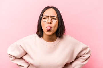 Young hispanic woman isolated on pink background funny and friendly sticking out tongue.