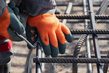 A worker uses steel tying wire to fasten steel rods to reinforcement bars. Close-up. Reinforced concrete structures - knitting of a metal reinforcing cage.