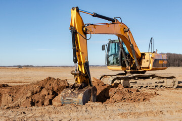 Obraz premium A powerful caterpillar excavator digs the ground against the blue sky. Earthworks with heavy equipment at the construction site.