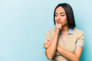 Young hispanic woman isolated on blue background looking sideways with doubtful and skeptical expression.