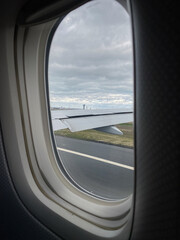 Fototapeta premium Airplane window seat view of airplane wing and airport runway with a cloudy sky