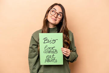 Young caucasian woman holding a bio placard isolated on beige background dreaming of achieving...