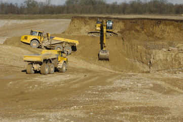 Yellow dump trucks and excavator are working in gravel pit