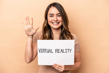 Fototapeta premium Young caucasian woman holding a virtual reality placard isolated on beige background smiling cheerful showing number five with fingers.