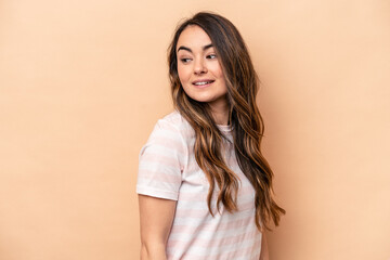 Obraz premium Young caucasian woman isolated on beige background looks aside smiling, cheerful and pleasant.