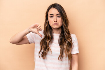 Fototapeta premium Young caucasian woman isolated on beige background showing a dislike gesture, thumbs down. Disagreement concept.