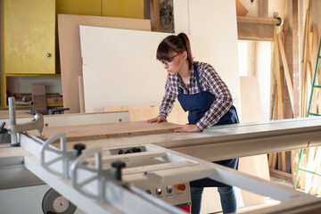 Carpenter woman using sliding table saw in her workshop