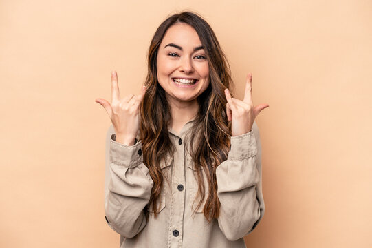 Young caucasian woman isolated on beige background showing a horns gesture as a revolution concept.