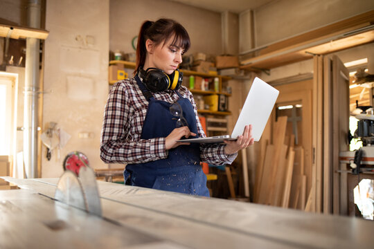 Carpenter woman using laptop with blueprints and planning work in her carpentry workshop - Powered by Adobe