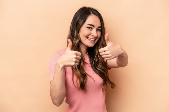 Young caucasian woman isolated on beige background raising both thumbs up, smiling and confident.