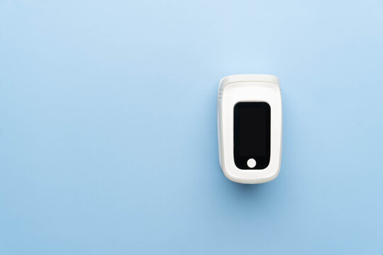 Pulse oximeter finger digital device for measure oxygen saturation in blood and pulse rate on blue background. Monitor health of people with pneumonia, anemia or heart failure.