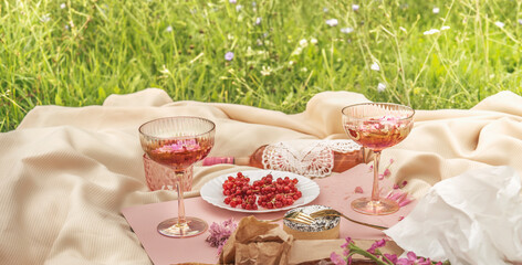 Picnic with champagne glasses, wine, cheese and red currants at pale beige blanket on the grass....