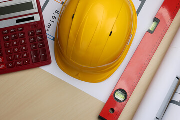 Construction drawings, safety hat, calculator and bubble level on wooden table, flat lay