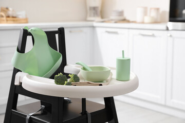 Fototapeta na wymiar High chair with broccoli and set of baby tableware on tray indoors