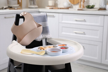 High chair with food in baby tableware on tray indoors