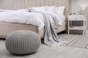 Stylish bedroom interior with knitted pouf and furniture