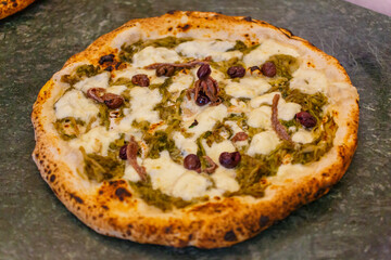 Pizza napoletana con scarole, mozzarella di bufala, olive e acciughe servita in una pizzeria