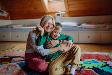 Happy boy with Down syndrome sitting on floor and hugging with his grandmother at home.