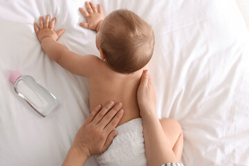 Mother massaging her cute baby with oil on bed, closeup