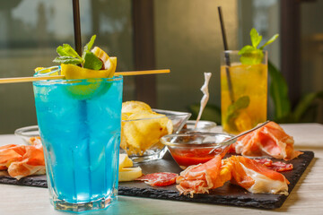 Aperitivo servito in un bar con due cocktail, patatine, crostini, bruschette con prosciutto crudo, arachidi, olive, formaggi, salame e salsa bbq