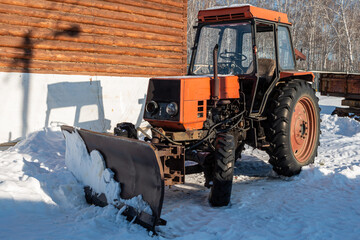 Orange wheeled snow plow tractor with blade in winter